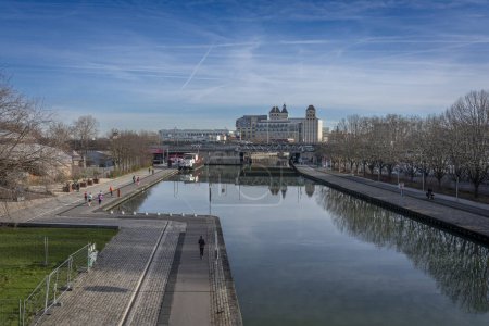 Photo for Paris, France - 01 27 2024: La Villette Park. View of the Canal of the Basin from the bridge of Flander with reflects and the park, sky, bridge, buildings and Les Grands Moulins of Pantin - Royalty Free Image