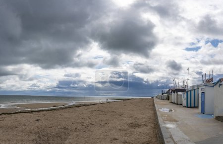 Langrune-Sur-Mer, France - 07 26 2023:  View of the sea, the jetty and people walking on the beach with a cloudy sky