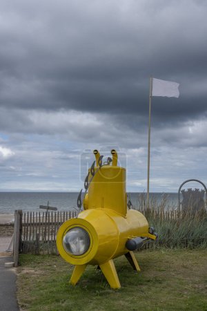 Ein gelbes U-Boot, eine weiße Flagge, der Strand und das Meer bei bewölktem Himmel