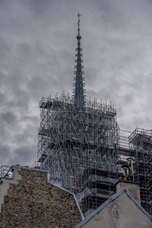 Paris, France - 02 15 2024: Notre Dame de Paris. View of the spire topped with the golden rooster of Notre-Dame cathedral emerging from the immense scaffolding of metal tubes