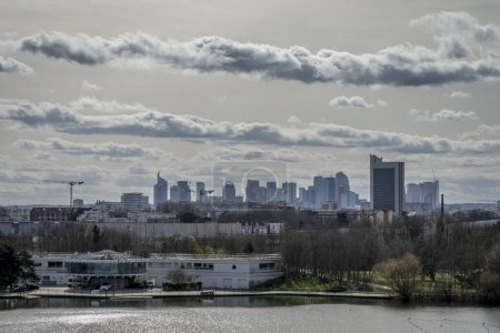 Gennevilliers, France - 03 16 2024: Chanteraines park. Nature in bloom in spring season. View of the artificial pond and the towers of La Defense district behind