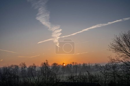 Sky Background. Detail view of a blue sky with colored clouds and aircraft trail at sunrise