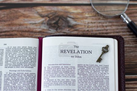 Revelation Bible Book with ancient key and magnifying glass on wooden background. Top table view. Christian concept of searching Scriptures, biblical prophecy, hope for second coming of Jesus Christ.