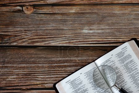 Bibelbuch mit Lupe auf Holztisch. Ansicht von oben. Kopierraum. Suchen, studieren, lesen christliche Schriften biblisches Konzept.