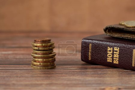 Stapel Münzgeld, Bibelbuch und alte Brieftasche auf einem Holztisch. Kopierraum, eine Nahaufnahme. Christliches biblisches Konzept des Zehnten, Gebens und religiösen Opfers.