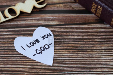 Photo for I love you-God, handwritten text on heart-shaped note and closed holy bible book on a wooden table. A closeup. Christian concept of love and hope in Jesus Christ. - Royalty Free Image