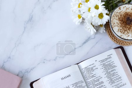 Prophet Isaiah open bible book with cup of coffee, flowers, and notebook on white marble background. Top view. Copy space. Old Testament prophecy study, reading Christian Scriptures, biblical concept.