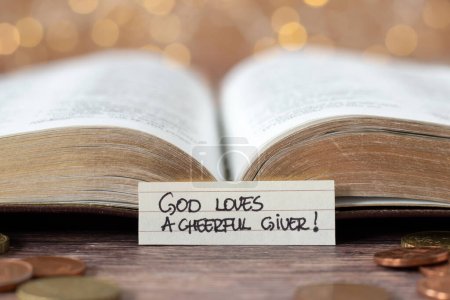 Photo for God loves a cheerful giver, handwritten text note in front of open holy bible book and golden coin money with bokeh background. Christian biblical concept of giving, tithing, and religious offering. - Royalty Free Image