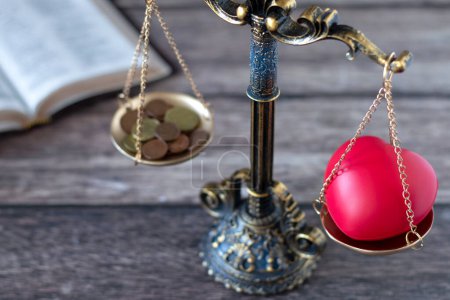 Photo for Balance scales with red heart shape and coins with holy bible book in the background. Selective focus. Christian priorities, justice, tithing, giving, love, or money concept. - Royalty Free Image