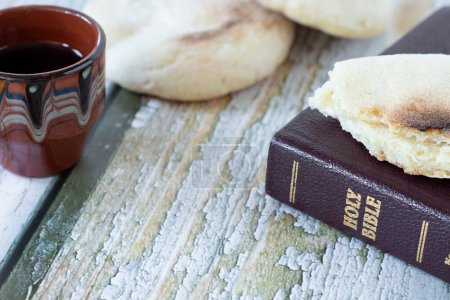 Brot und Wein mit geschlossener Bibel auf Holztisch. Christliches biblisches Konzept von geistlichem Essen und Trinken.