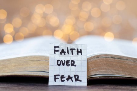 Faith over fear, handwritten quote and open holy bible book with bokeh light background. Christian biblical concept of faith and trust in God Jesus Christ. Close-up.