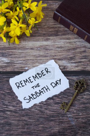 Souvenez-vous du jour du sabbat, note manuscrite avec la bible sainte, clé antique, et des fleurs sur la table en bois. Obéissance chrétienne, observance des commandements, repos pour le peuple de Dieu, concept biblique.