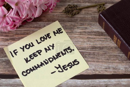 If you love Me keep My commandments, Jesus Christ, handwritten quote with ancient key, holy bible book and flowers on wood. Close-up. Christian obedience to God, 10 commandments, biblical concept.