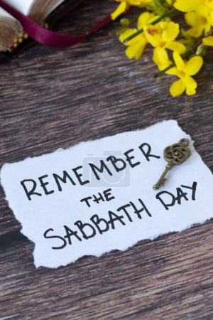 Remember the Sabbath Day, handwritten quote with antique key, holy bible, and flowers on wooden table. Christian obedience, keeping the commandments, rest for the people of God, biblical concept.