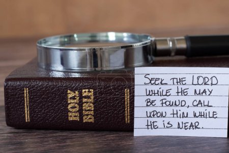Seek the LORD while He may be found, handwritten quote with magnifying glass and closed holy bible book. Close-up. Biblical concept of Christian study, prayer and obedience to God Jesus Christ.