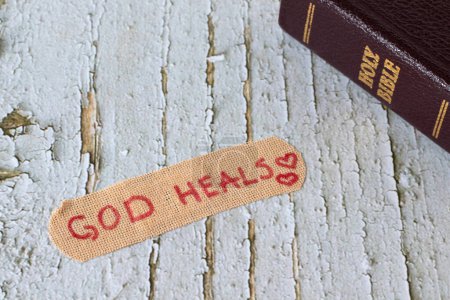 God heals, handwritten text on bandage with closed holy bible book on wooden background. Christian biblical concept of mercy, love, compassion and grace.