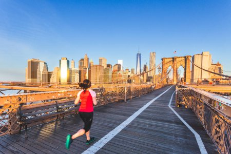 Téléchargez les photos : Un coureur sur le fond du pont de Brooklyn et le ciel bleu au lever du soleil dans le paysage urbain de New York. - en image libre de droit