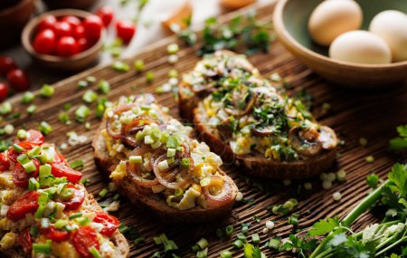 Téléchargez les photos : Sandwichs aux œufs brouillés et divers légumes, se concentrer sur le sandwich avec des rondelles d'oignon sur une planche en bois - en image libre de droit