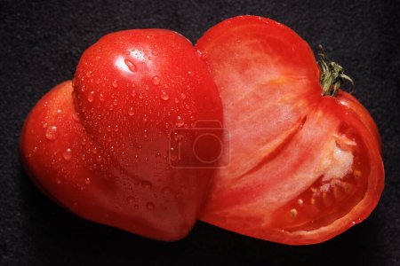 Téléchargez les photos : Tomate en forme de coeur coupé en deux sur un fond noir. Tomate de Saint-Valentin - en image libre de droit