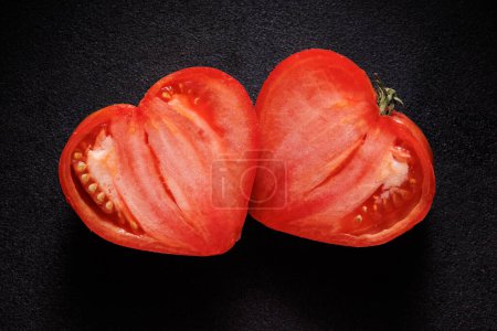 Foto de Tomate en forma de corazón cortado por la mitad sobre un fondo negro. Tomate de San Valentín - Imagen libre de derechos
