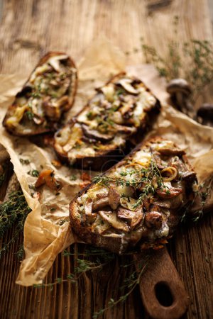 Photo for Grilled sandwiches, toasts with forrest mushrooms Suillus luteus, cheese and thyme herb on a wooden table, close up view - Royalty Free Image