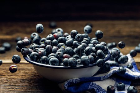 Photo for Fresh blueberries in an enamel bowl on a wooden rustic table, close up view. Levitating blueberries - Royalty Free Image