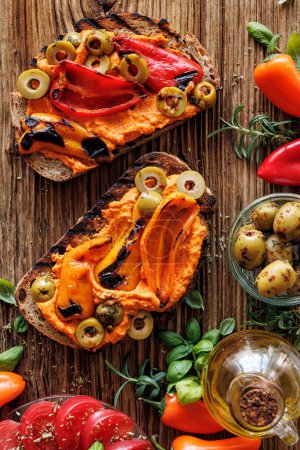 Photo for Sandwiches with pepper hummus, grilled peppers and green olives  on a wooden rustic table, top view - Royalty Free Image