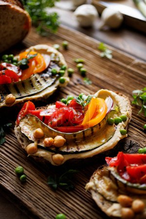 Foto de Sandwich de cara abierta con hummus y verduras en una tabla de madera, vista de cerca. Comida vegetariana saludable - Imagen libre de derechos