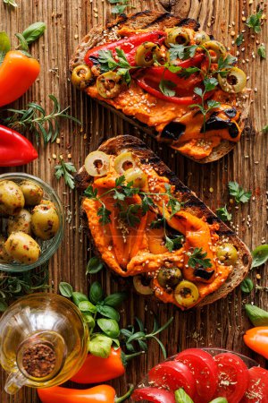 Photo for Traditional sourdough bread sandwiches with hummus and grilled peppers, green olives sprinkled with fresh parsley on a wooden rustic table, top view - Royalty Free Image