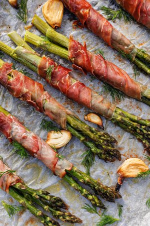 Photo for Roasted green asparagus wrapped with ham sprinkled with herbs, close up view - Royalty Free Image