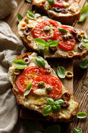 Photo for Grilled sandwiches, bruschettes made of sourdough bread with the addition of cheese,  tomatoes and olives sprinkled with herbs, close up view - Royalty Free Image