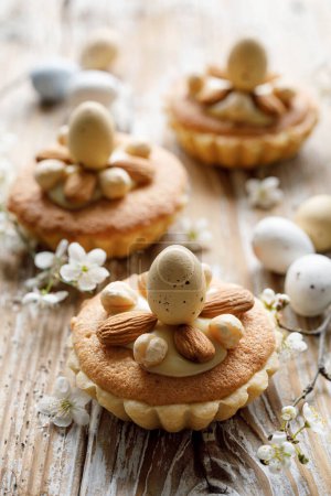 Téléchargez les photos : Mini tartes décorées avec des amandes et des noix et un oeuf en chocolat sur une table en bois décorée avec des fleurs de printemps, vue rapprochée. Une idée pour un délicieux dessert de Pâques - en image libre de droit