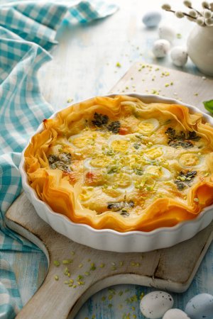 Photo for Quiche made of phyllo dough with addition of hard boiled quail eggs and herbs in a baking dish, close up view. - Royalty Free Image
