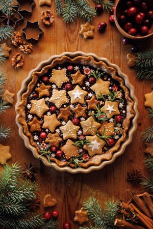Photo for Gingerbread and chocolate tart decorated gingerbread cookies in the star shapes, cranberries and rosemary in a baking dish on a wooden table, top view. Christmas tart. - Royalty Free Image