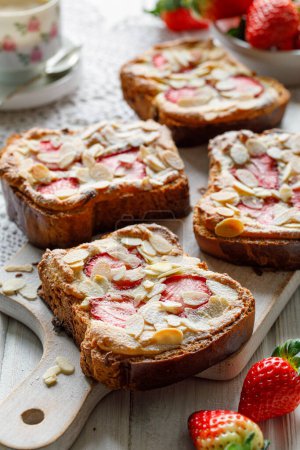 Photo for Bostock a French pastry made of sliced brioche with frangipane cream and fresh strawberries  served on a white board, close up view. Delicious breakfast or dessert - Royalty Free Image