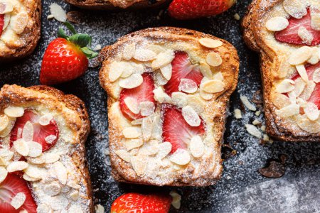 Photo for Bostock a slice of brioche pastry with frangipane cream, strawberries and almond flakes, sprinkled with powdered sugar on a black background, close up view - Royalty Free Image