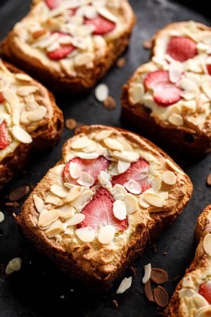 Photo for Bostock a slice of brioche pastry with frangipane cream, strawberries and almond flakes on a black background, close up view - Royalty Free Image