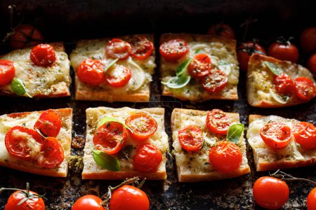 Téléchargez les photos : Toasts à la baguette au fromage mozzarella et tomates cerises assaisonnés de basilic frais sur fond sombre, vue rapprochée - en image libre de droit