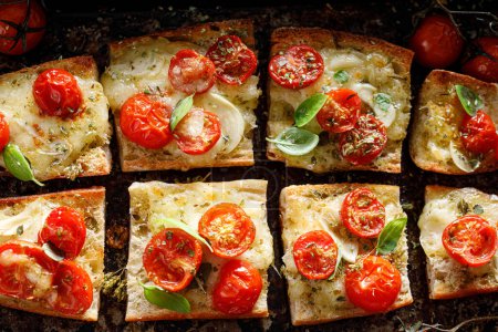 Téléchargez les photos : Toasts à la baguette au fromage mozzarella et tomates cerises assaisonnés de basilic frais sur fond sombre, vue rapprochée - en image libre de droit