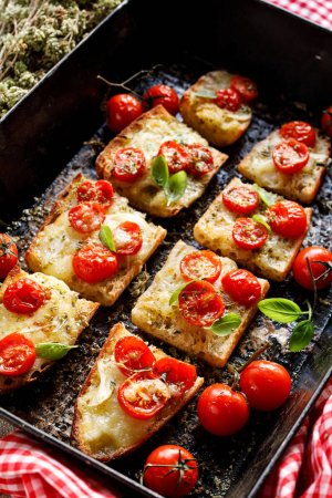 Foto de Tostadas de baguette con queso mozzarella y tomates cherry sazonados con hierbas en una lata para hornear, vista de cerca - Imagen libre de derechos