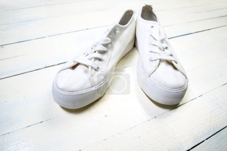 Foto de Zapatillas jóvenes blancas con blanco desatado los cordones sobre fondo de madera - Imagen libre de derechos