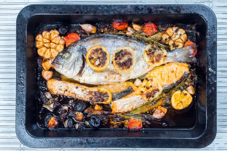 Photo for Sea bream and salmon in a black pan with vegetables and spices - Royalty Free Image