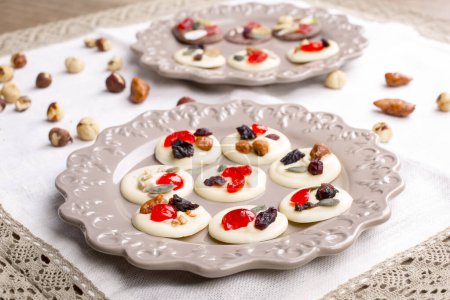 Foto de Pasteles de chocolate blanco con frutas confitadas, frutos secos y semillas en mesa de madera - Imagen libre de derechos