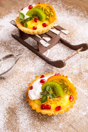 Téléchargez les photos : Gâteau sucré aux fruits sur l'arrangement de Noël avec traîneaux et neige - en image libre de droit