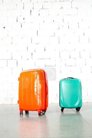 Foto de Bolsas de viaje naranjas y verdes sobre fondo de ladrillo blanco - Imagen libre de derechos