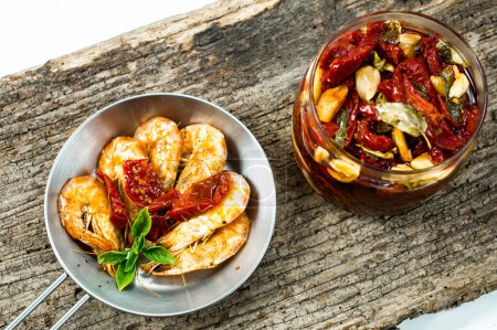 Téléchargez les photos : Crevettes dans la casserole avec tomates sèches sur fond en bois - en image libre de droit