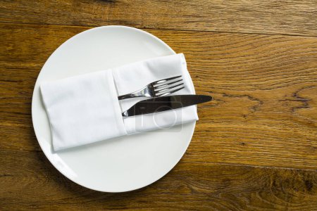 Téléchargez les photos : Assiette vide avec couverts, fourchette et couteau sur serviette sur fond bois. - en image libre de droit