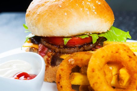 Téléchargez les photos : Grand burger de bœuf avec rondelles d'oignon et frites. Focus sélectif sur le burger - en image libre de droit