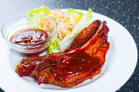 Téléchargez les photos : Porterhouse grillé tendre ou steak t-bone servi avec une salade d'herbes vertes fraîches accompagnée d'un barbecue ou d'une sauce tomate ketchup - en image libre de droit