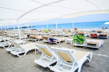 Foto de Tumbonas de plástico blanco en la playa de arena bajo una gran sombrilla - Imagen libre de derechos